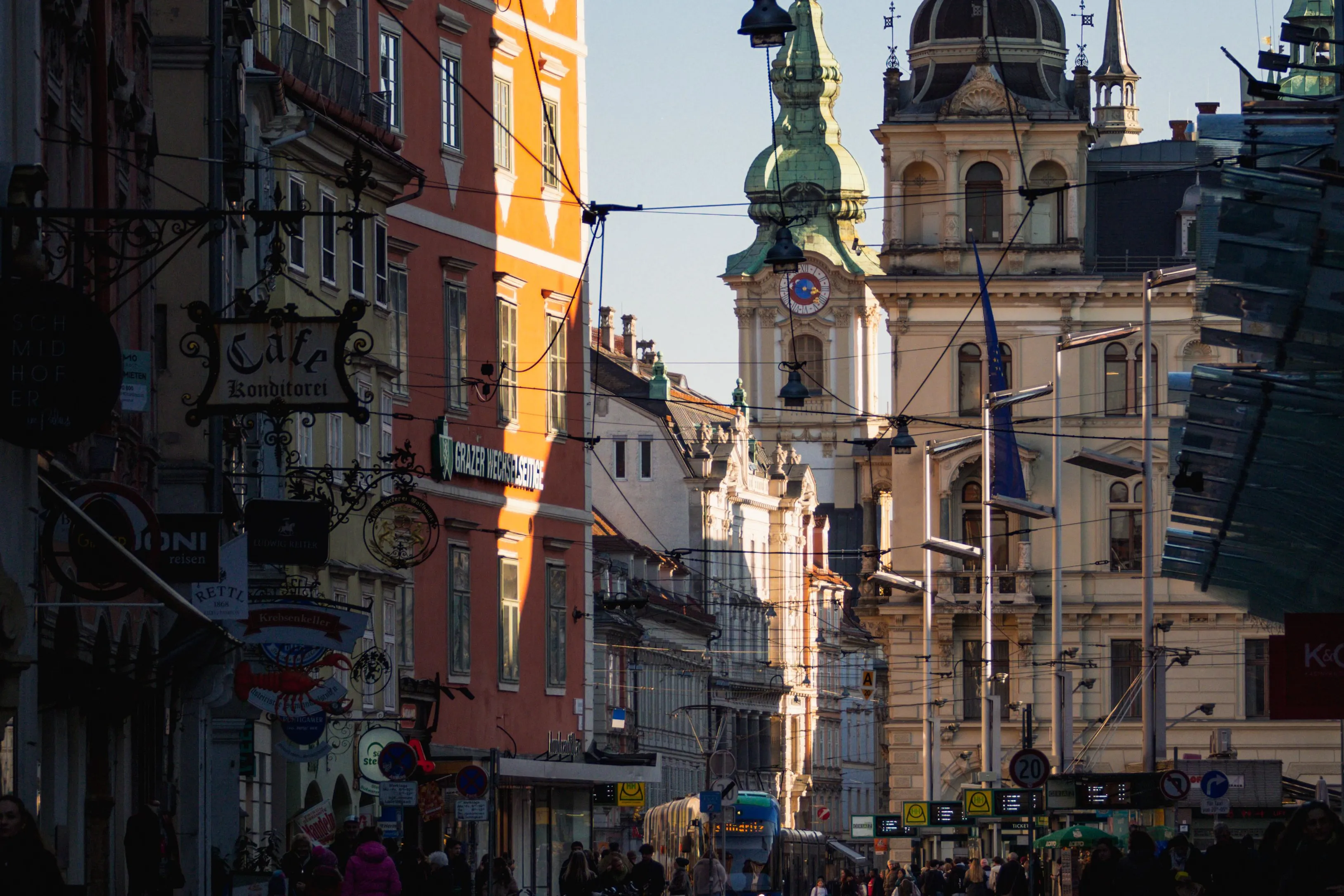 Altstadtstraße mit Straßenbahngleisen im Gegenlicht, am Ende das Rathaus und ein barocker Turm mit grüner Haube