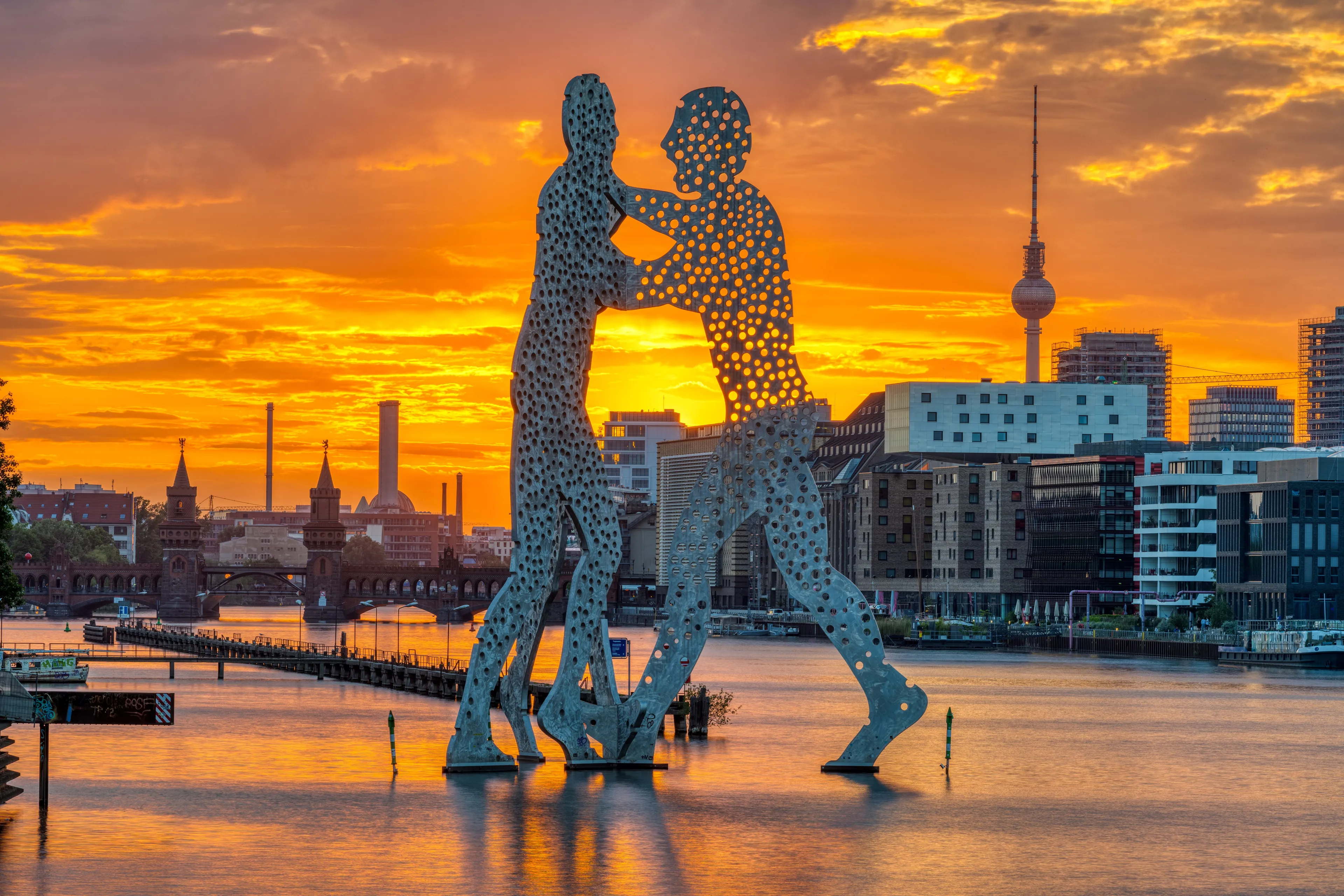 Molecule Man sculpture in the Spree at sunset, with the TV tower behind