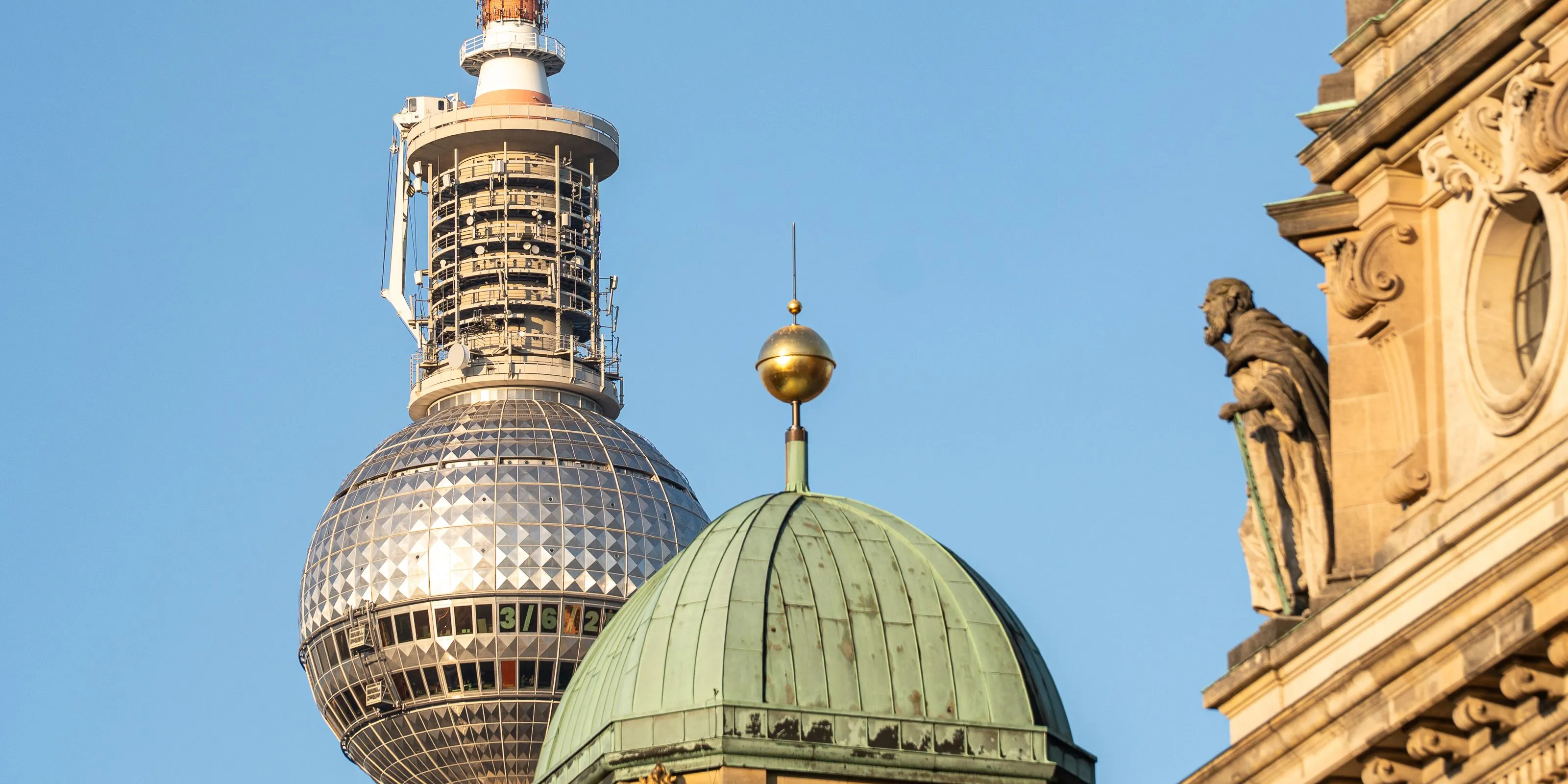 Dome and statue of Berlin Cathedral, with the TV tower behind in warm light