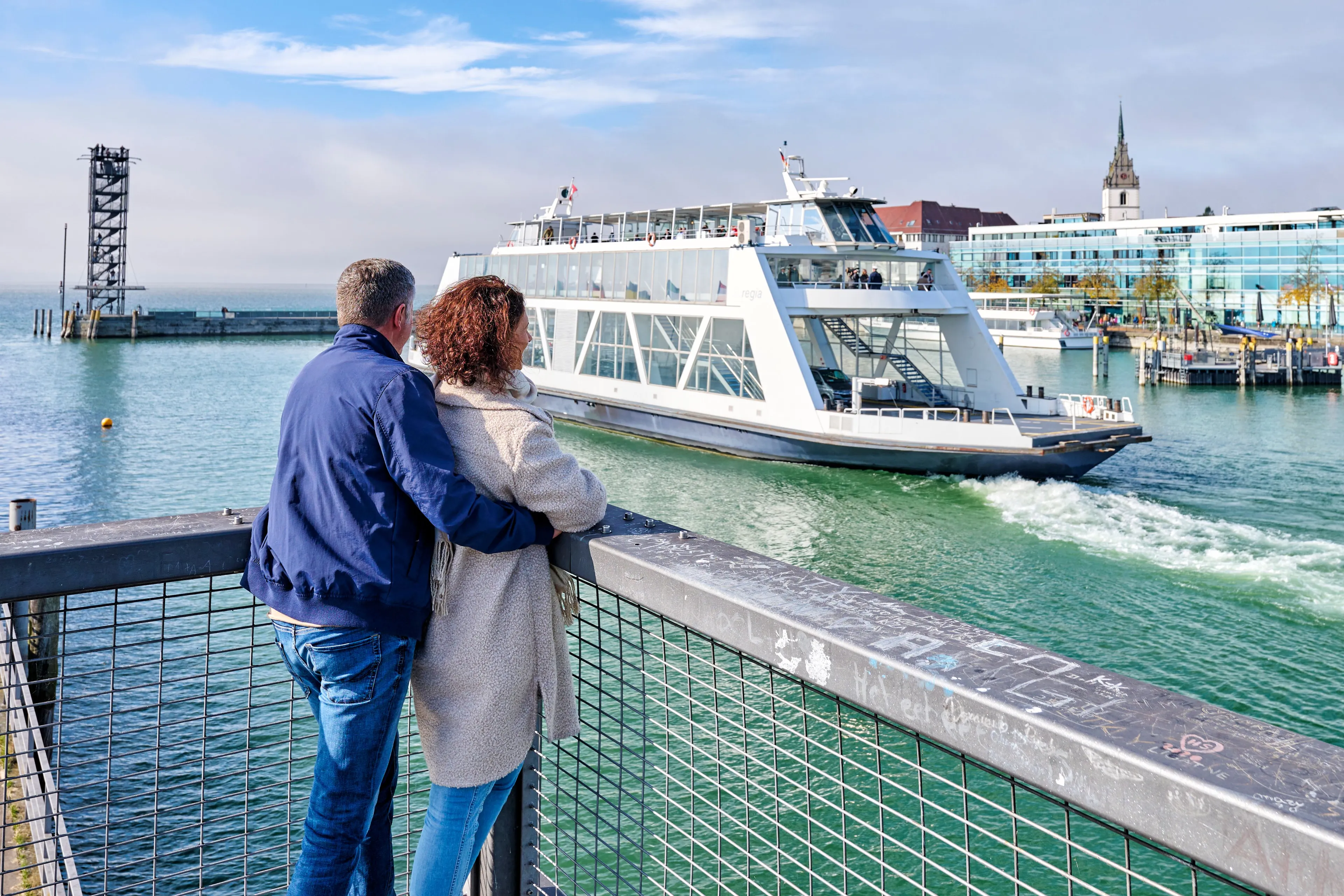 Couple on a pier watching a passenger ship in a Lake Constance harbour