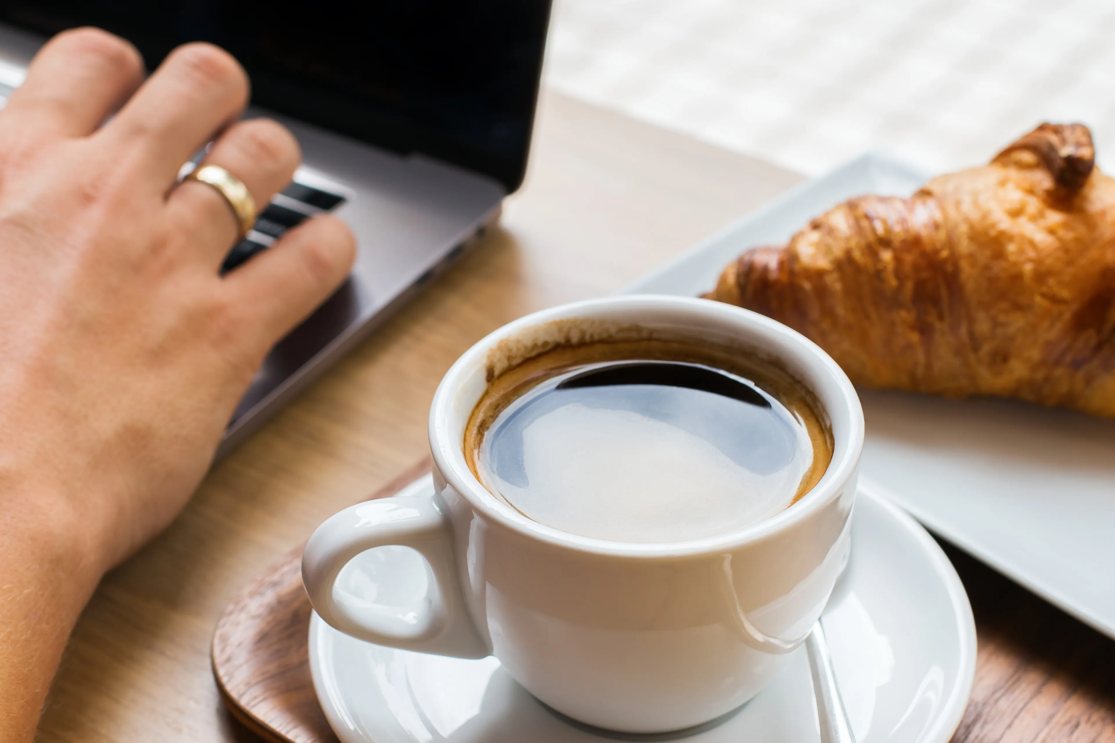 Hand auf einem Laptop neben Cappuccino und Croissant in einem Café