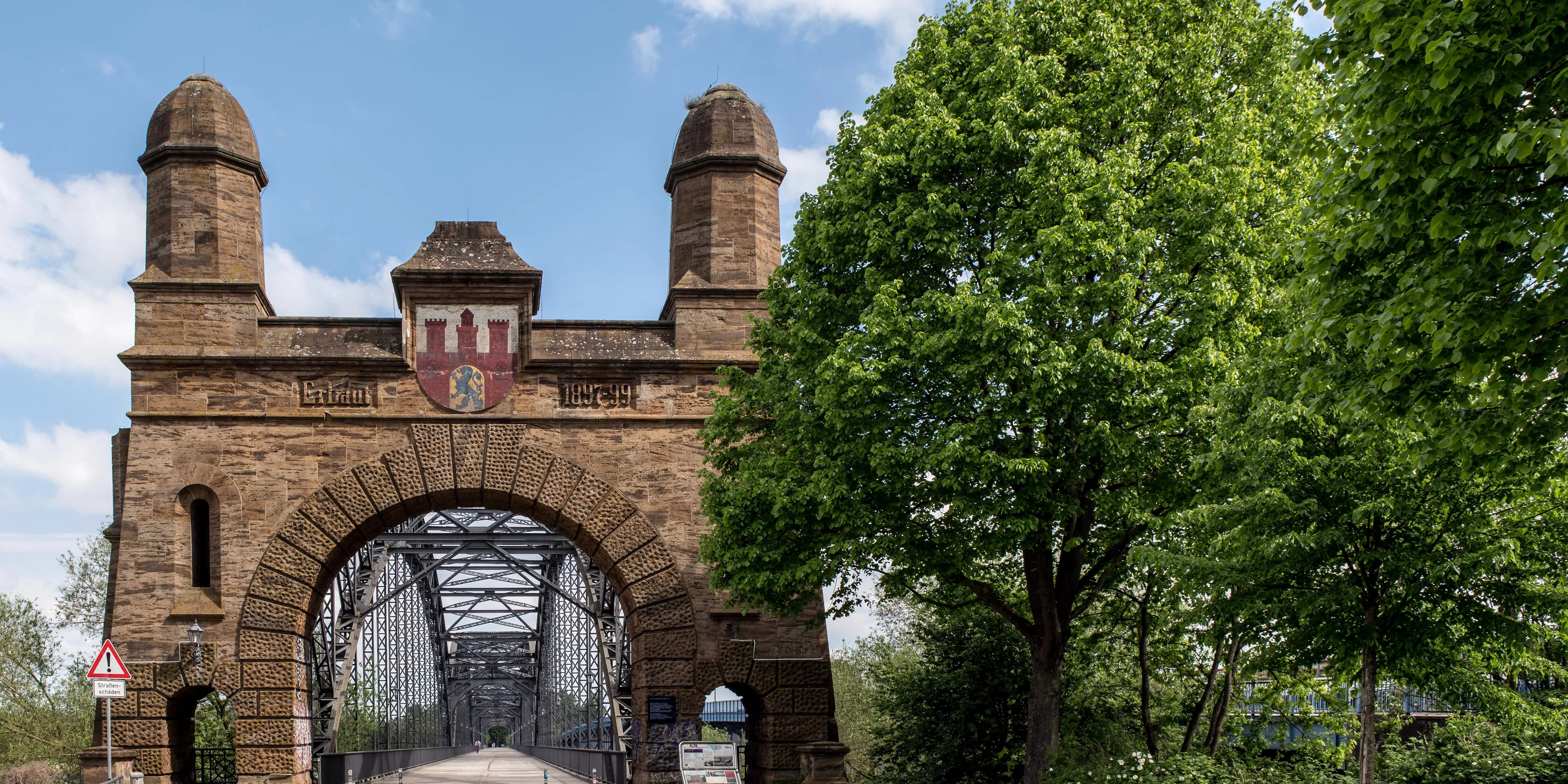 Sandstone gate with two towers and a coat of arms at the entrance of the Old Harburg Elbe Bridge, its steel trusses behind