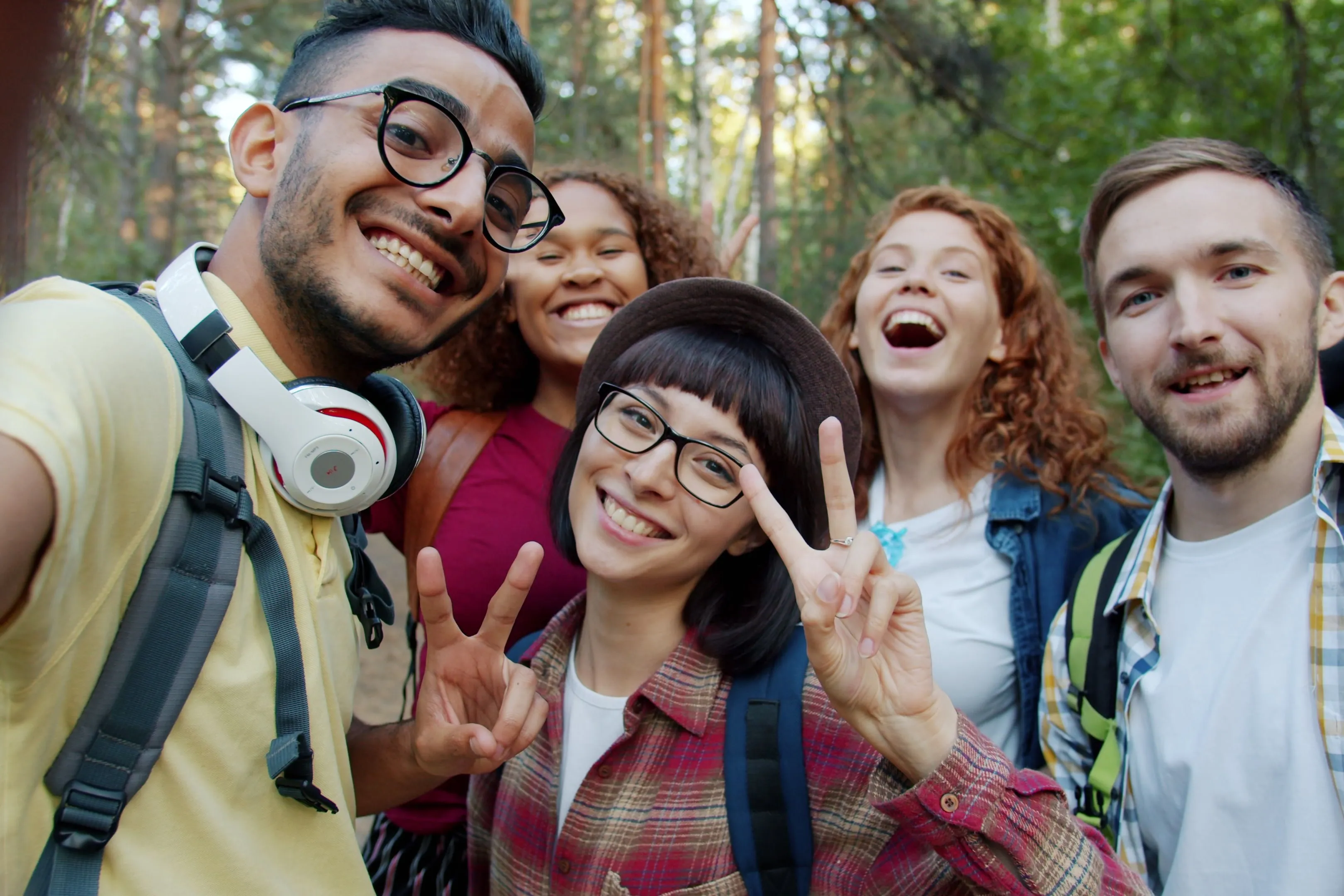 Gruppe lachender Freunde mit Rucksäcken beim Selfie im Wald