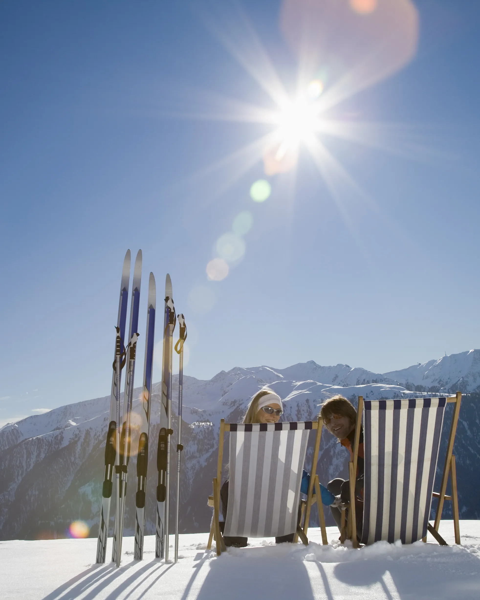 Zwei Liegestühle und Skier im Schnee vor einem Alpenpanorama