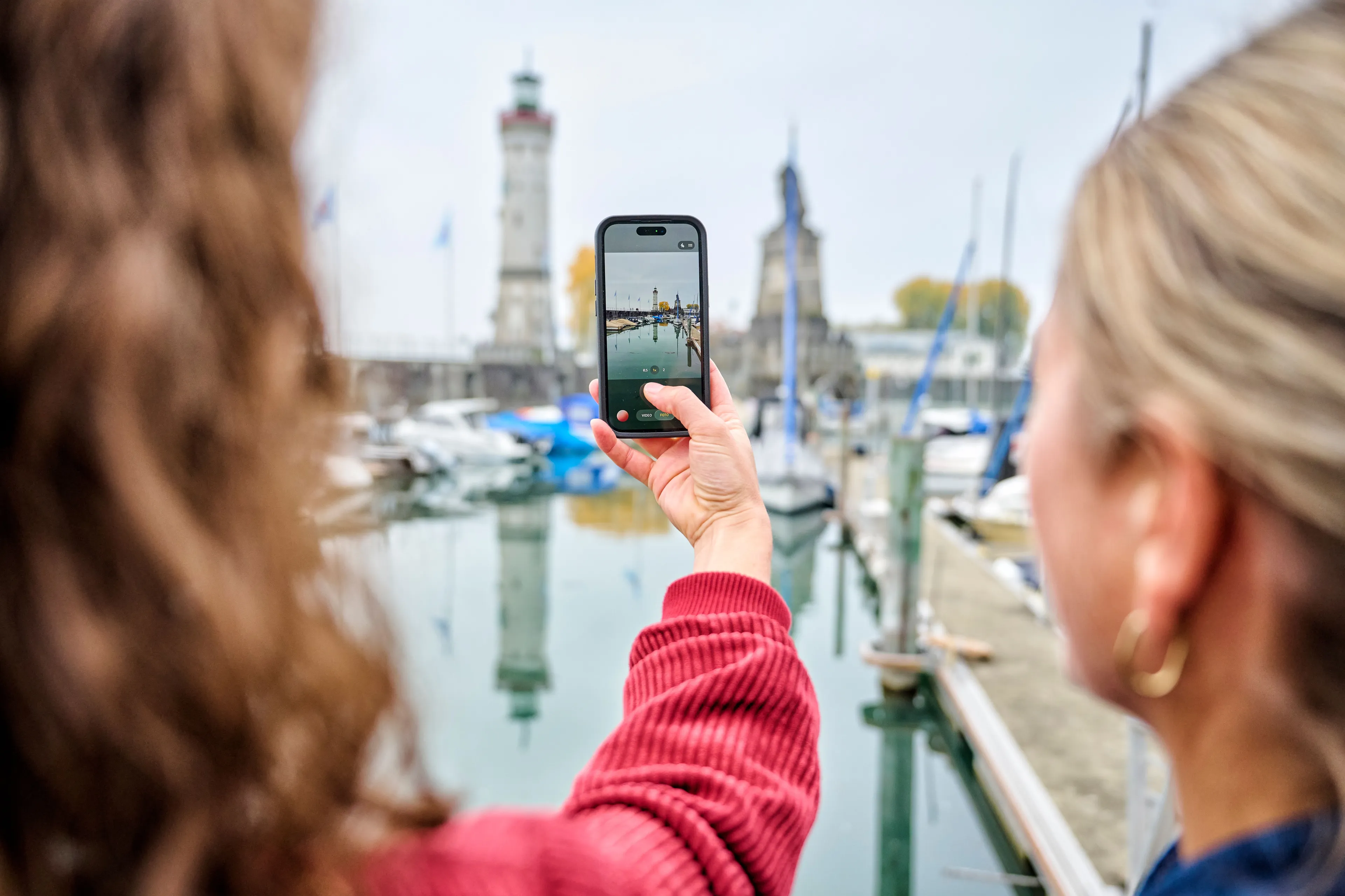 Zwei Freundinnen fotografieren den Hafen von Lindau mit Leuchtturm